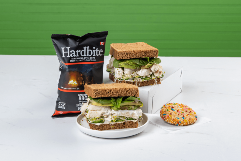Photo of two sandwiches, a bag of chips and a cookie.